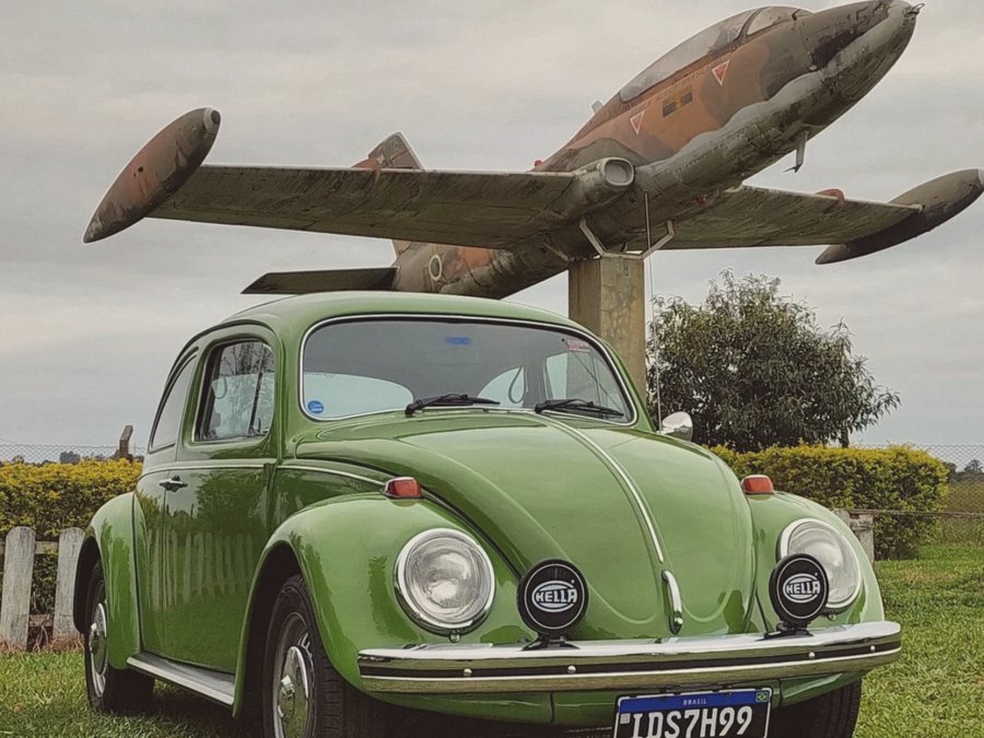 Fusca verde estacionado sob um avião em exposição